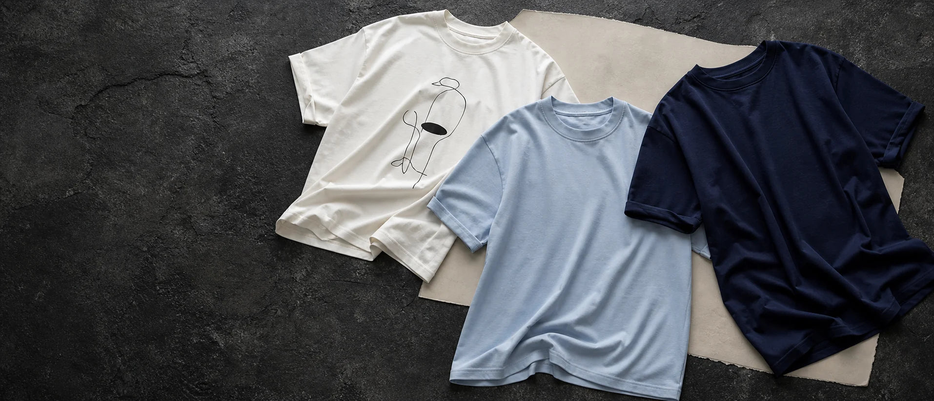 Three unbranded T-shirts arranged on a dark stone surface